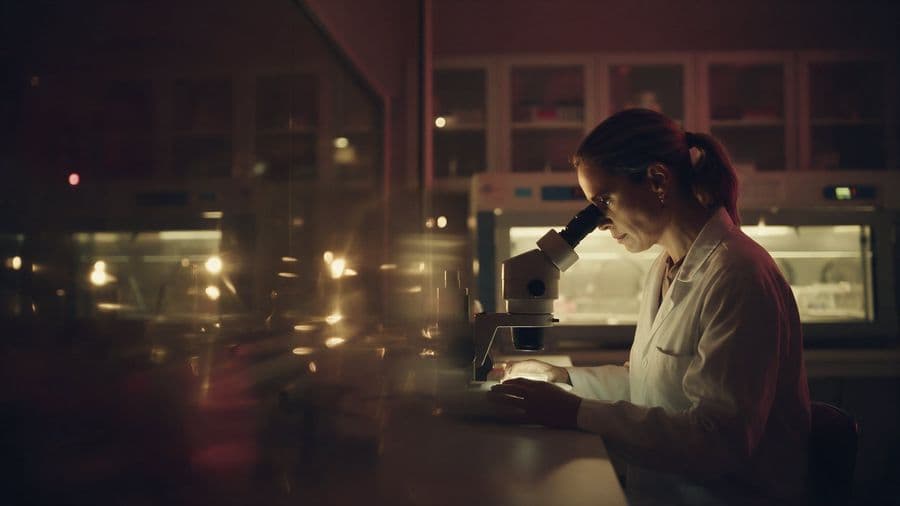 Embriologista de jaleco observa ao microscópio em um laboratório de reprodução humana